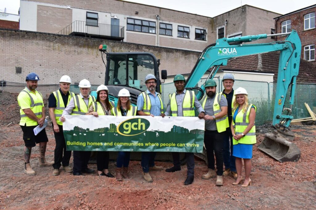 10 development partners stood on the site in front of a green digger