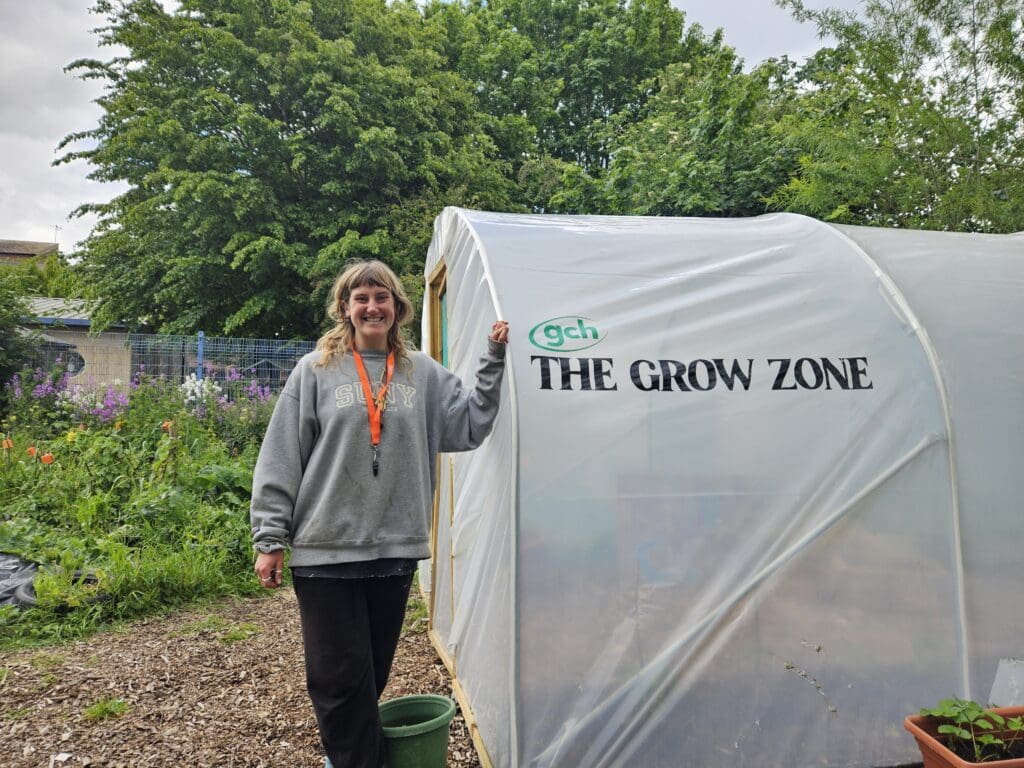 Project Grow at Kingsholm Primary School. image shows the Project Grow urban community farmer next to a polytunnel labelled The Grow Zone and GCH logo