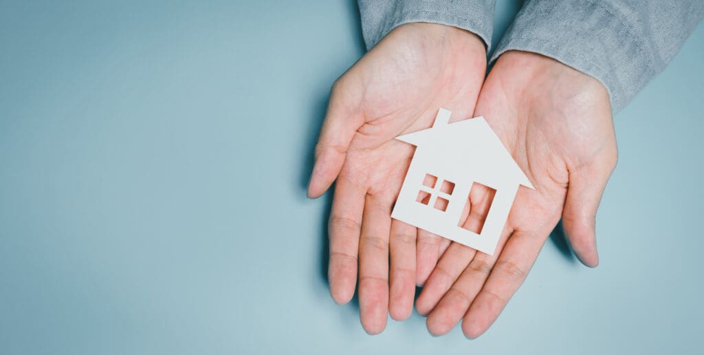hands holding paper house cutout, family home security awareness, housing protection idea, financial stability insight, safe shelter symbolism, community support concept