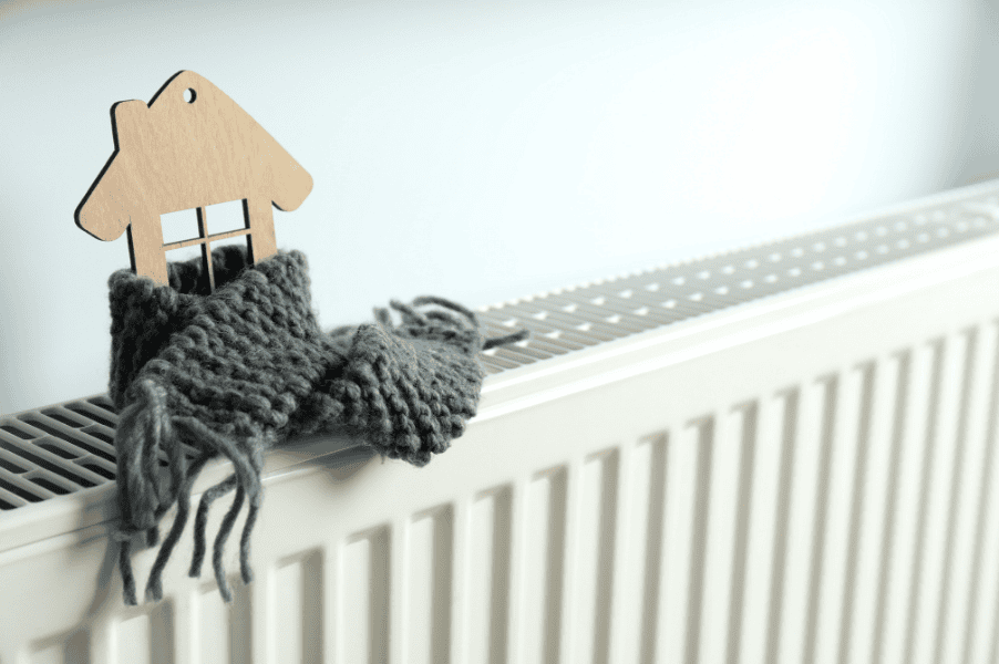Small wooden house wrapped in a small scarf on top of a radiator